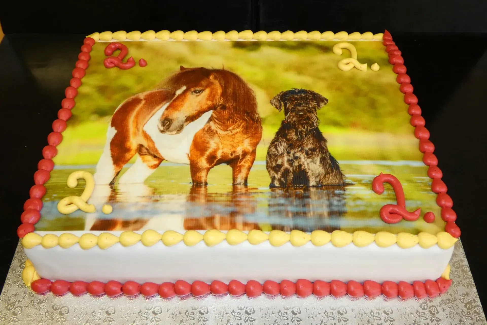 Verzierter Kuchen mit einer Pferde- und Hundeillustration, gelbem Zuckerguss und rot-weißem Rand.
