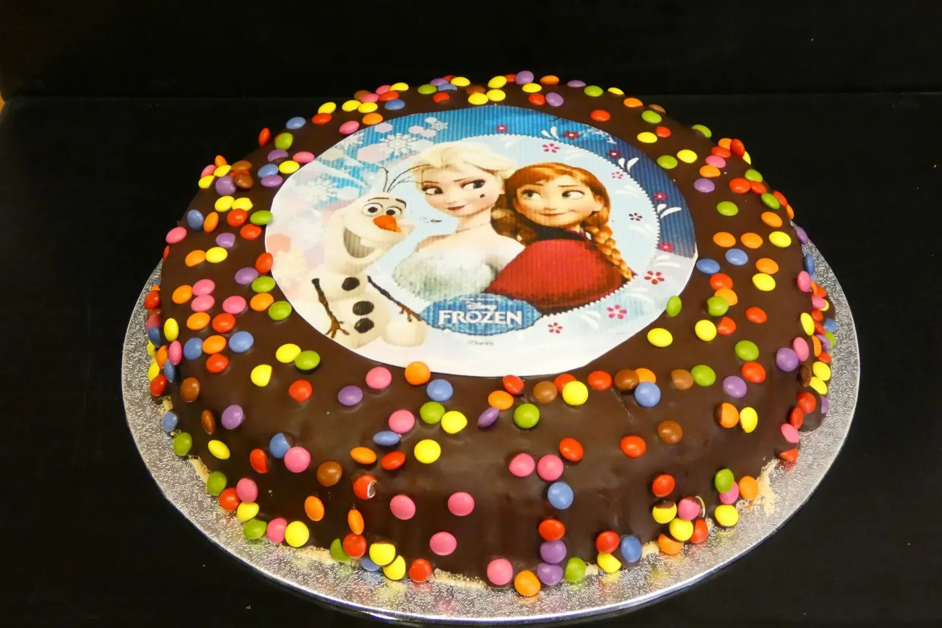 Schokoladenkuchen mit bunten Zuckerstreuseln und einer Eiskönigin-Figur als Tortenfigur auf einem silbernen Tablett