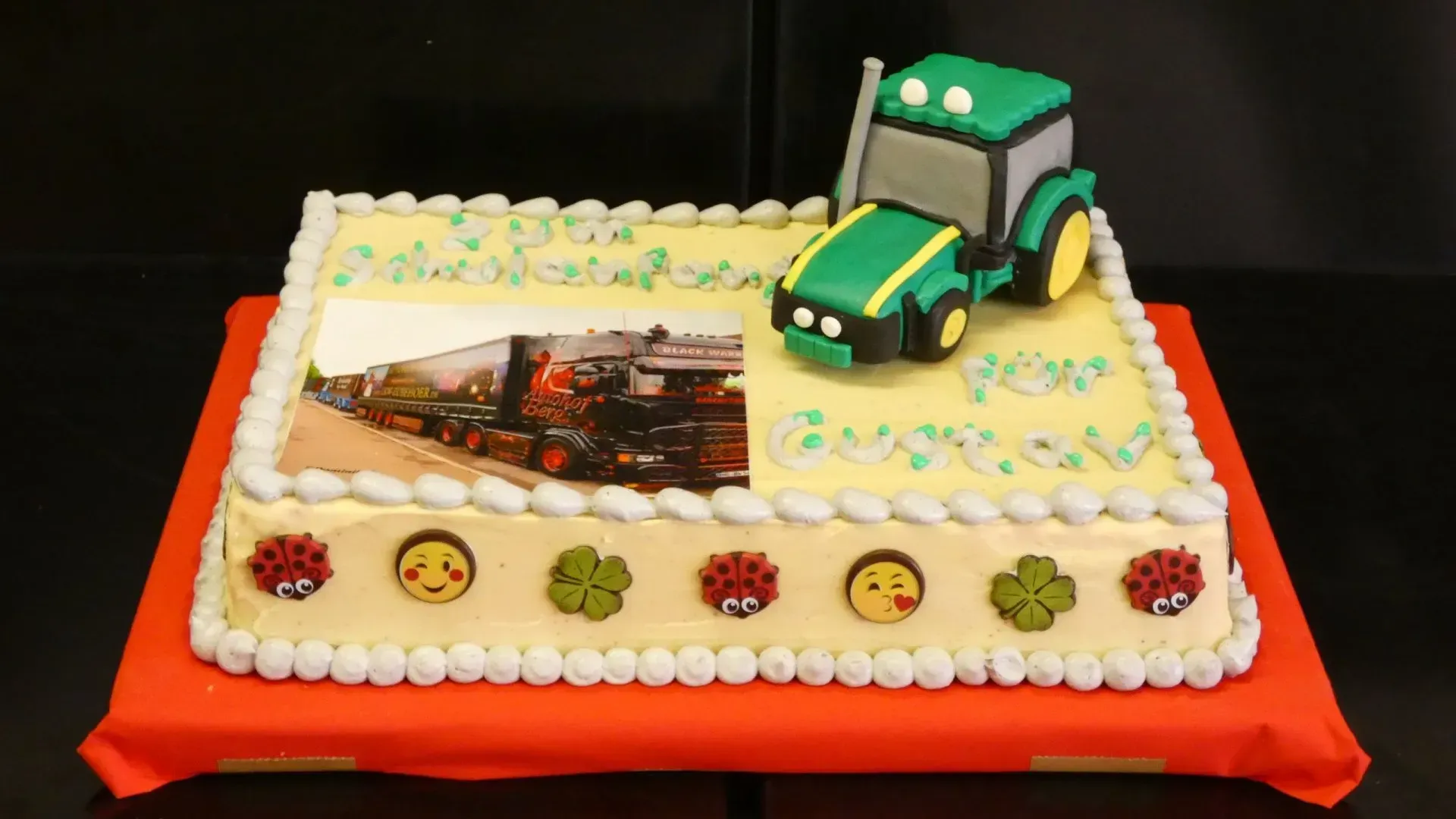 Verzierter Kuchen mit einem grünen Traktor als Tortenaufsatz auf rotem Brett