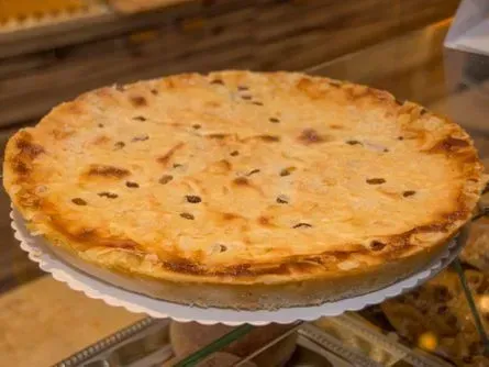 Ein goldbraun gebackener Kuchen auf einem weißen Ständer an der Theke einer Bäckerei.
