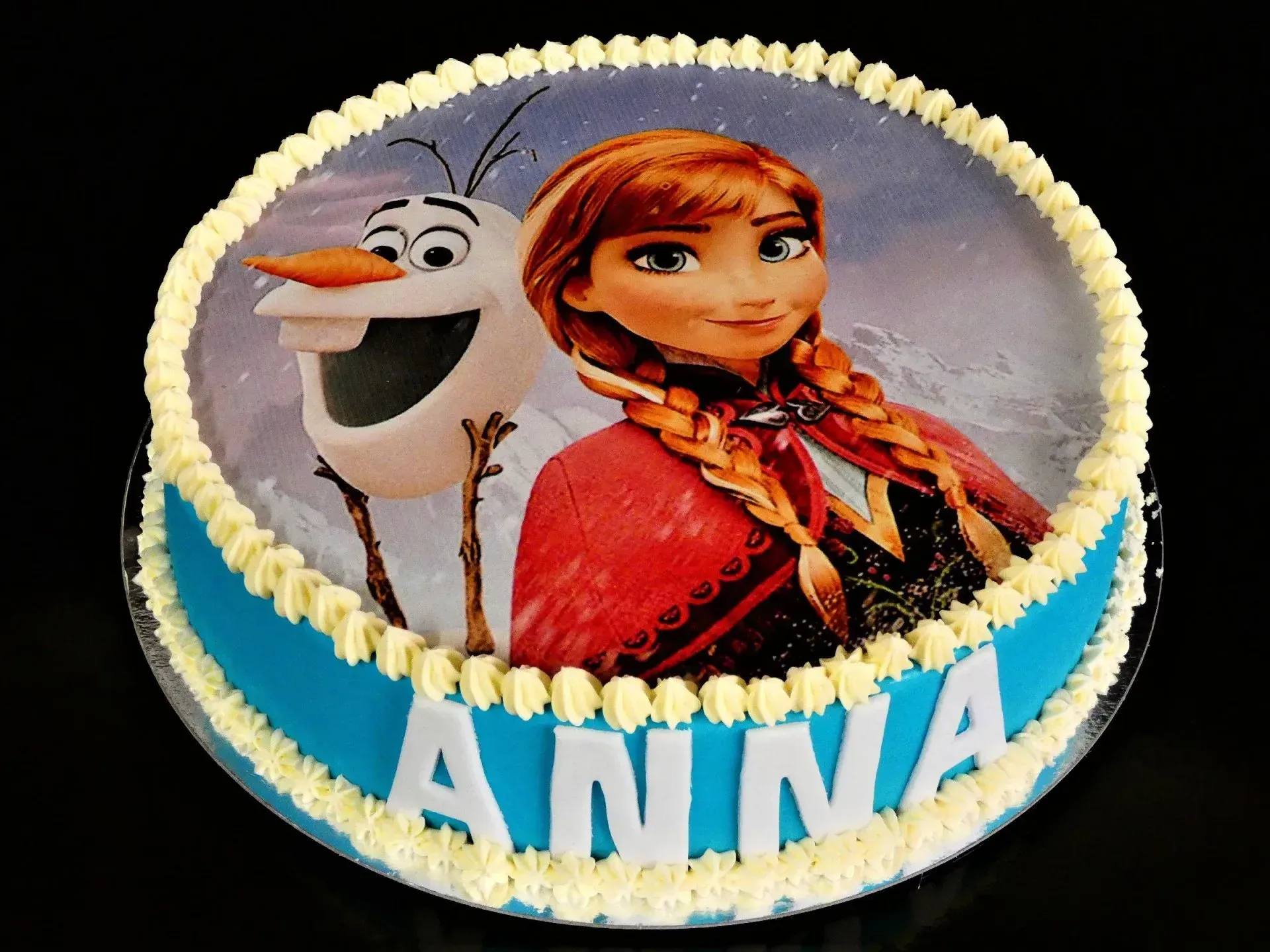 Torte im Frozen-Stil mit Anna und Olaf, blauer Glasur und dem Namen „ANNA“ auf der Vorderseite