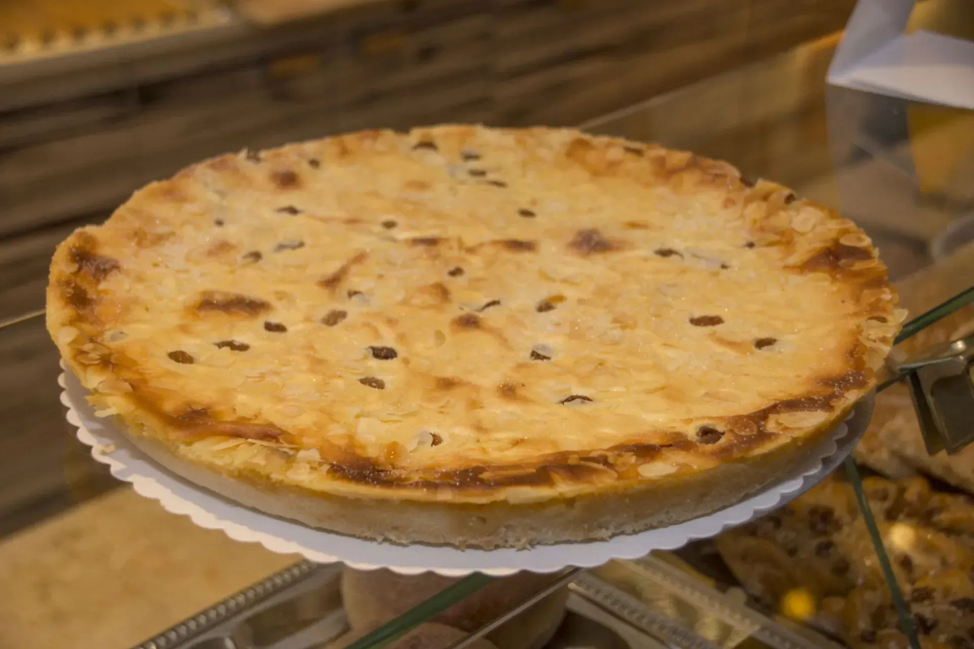 Eine große, goldbraun gebackene Torte auf einem Auslageständer in einer Bäckereivitrine