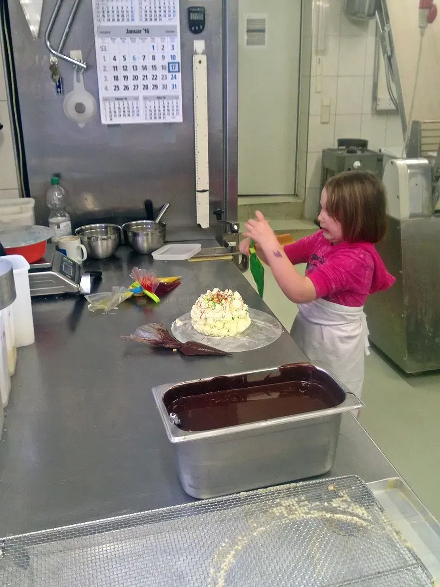 Ein Kind verziert einen Kuchen in einem Küchenvorbereitungsbereich; Backformen und -utensilien stehen auf der Arbeitsfläche.