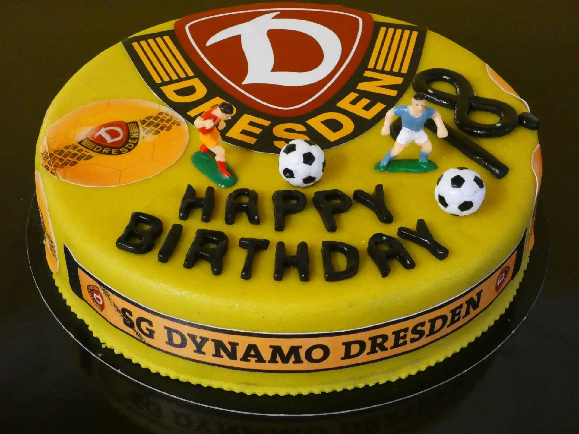Gelbe Geburtstagstorte mit dem Logo des FC Dynamo Dresden, Fußbällen und der Aufschrift „HAPPY BIRDAY“.