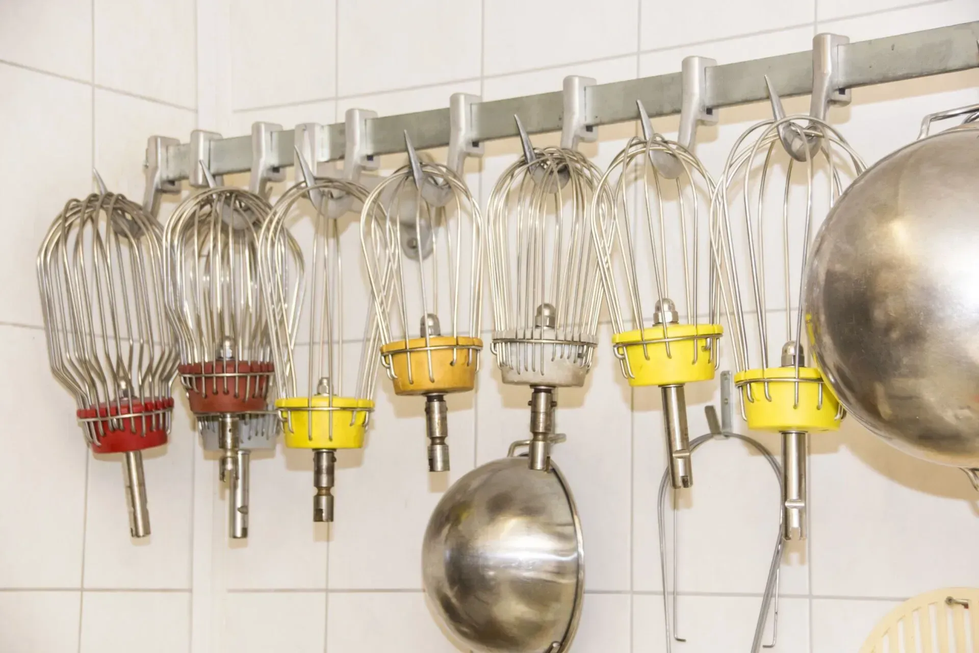 An der Wand montierte Reihe von Metall-Handmixern in einer Küche, mit gelben und roten Akzenten