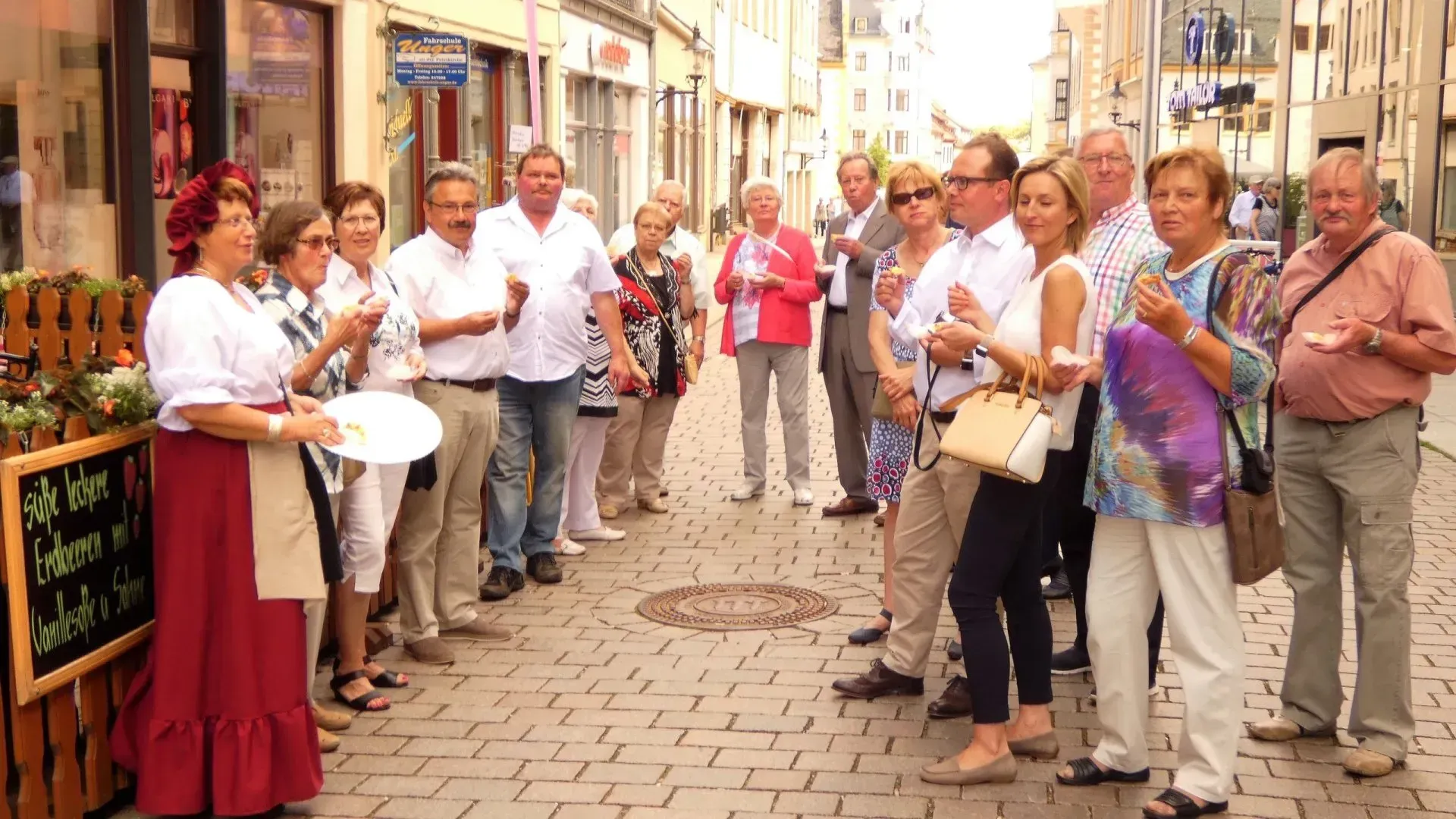 Gruppe Menschen auf Kopfsteinpflasterstraße, sprechen, halten Getränke und Zeitungen