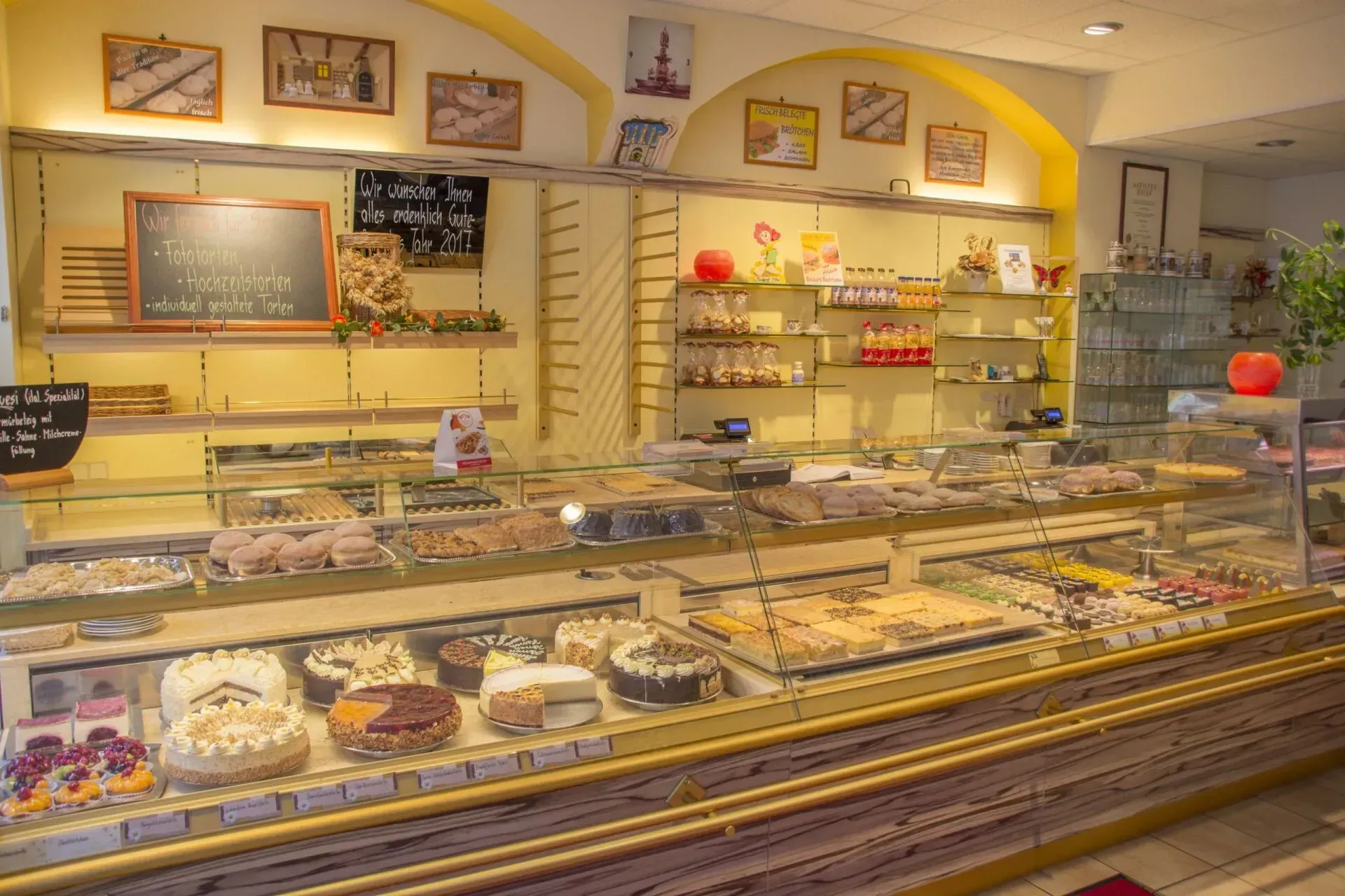 Auslage einer Bäckerei mit verschiedenen Gebäcksorten, Kuchen und Broten in einem warmen, gelben Ladeninterieur