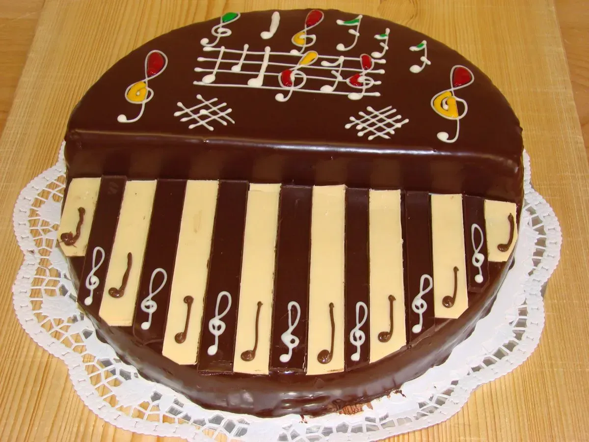 Schokoladenkuchen in Klavierform auf einem Deckchen, verziert mit weißen Noten und Klaviertasten.