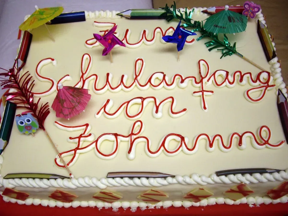 Verzierter Kuchen mit rotem Zuckerguss und der Aufschrift „Schulanfang von Johanna“ sowie bunten Schulfiguren.