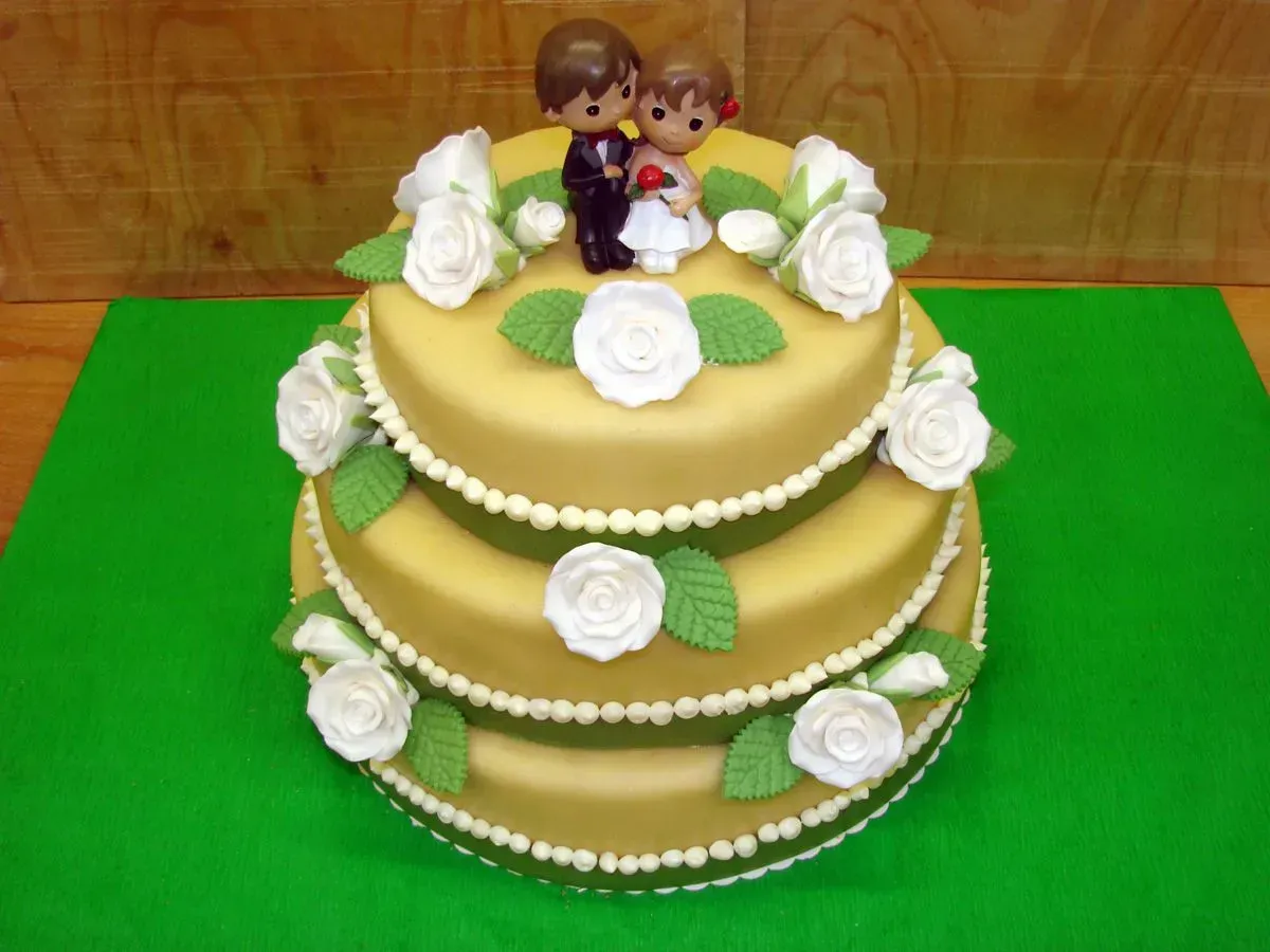 Dreistöckige grüne und goldene Torte, verziert mit weißen Rosen und Perlenrand, gekrönt von zwei Figuren