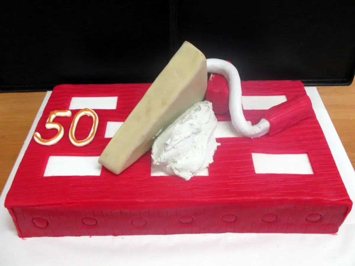 Roter Kuchen mit einer goldenen „50“, weißem Zuckerguss und einer beigen Keilverzierung obendrauf.