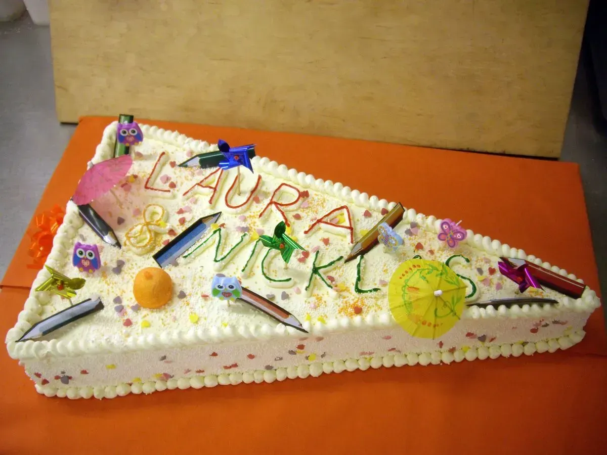Verzierter weißer Kuchen mit bunten Zuckerbuchstaben, Blumen und Fruchtscheiben auf einem orangefarbenen Tablett