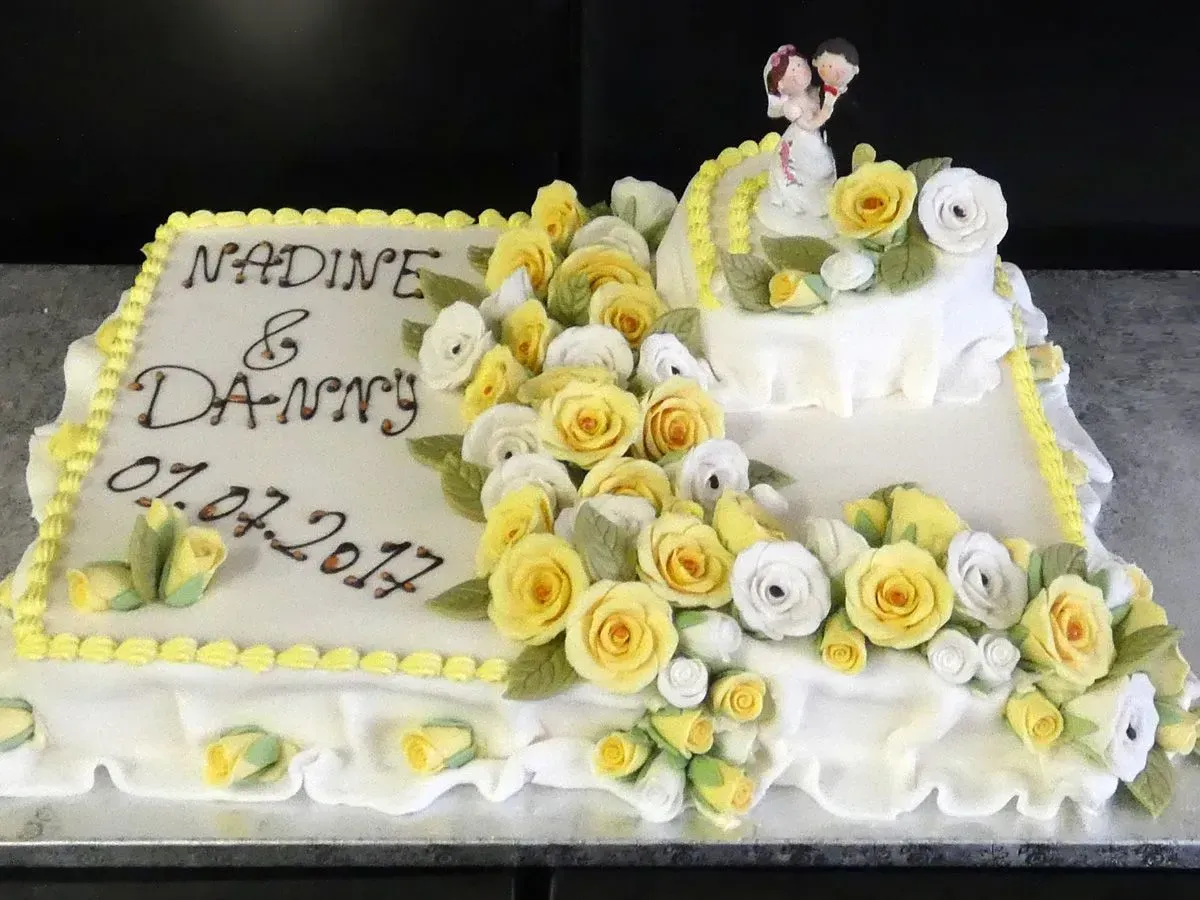 Weißer Kuchen, verziert mit gelben Rosen, mit der Aufschrift „Madin's D-Gurr“ und dem Datum 07.02.2022.