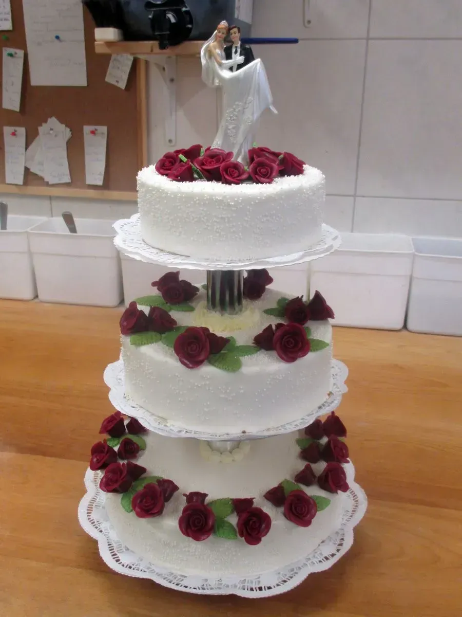 Dreistöckige weiße Hochzeitstorte mit roten Rosen und einer Brautfigur auf einem Tisch