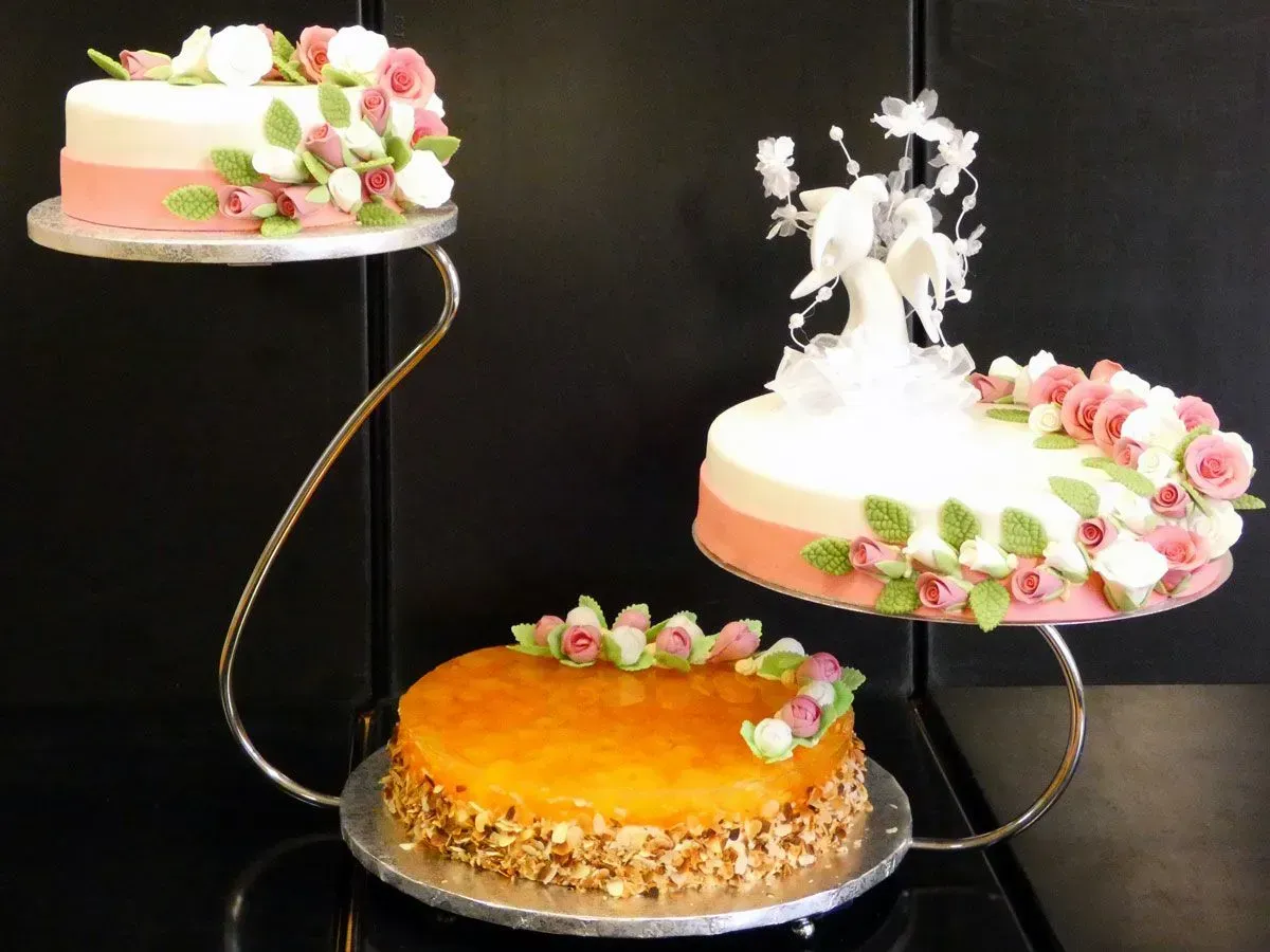 Dreistöckige Torten auf schwarzen Ständern, verziert mit Blumen und weißem Zuckerguss auf dunklem Hintergrund