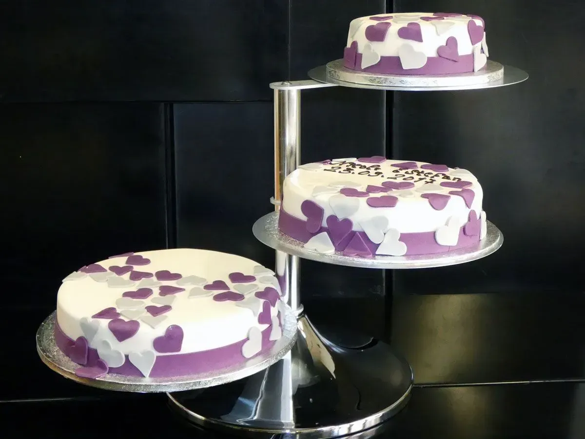 Drei lila-weiß glasierte Kuchen auf einem silbernen Etagere vor dunklem Hintergrund