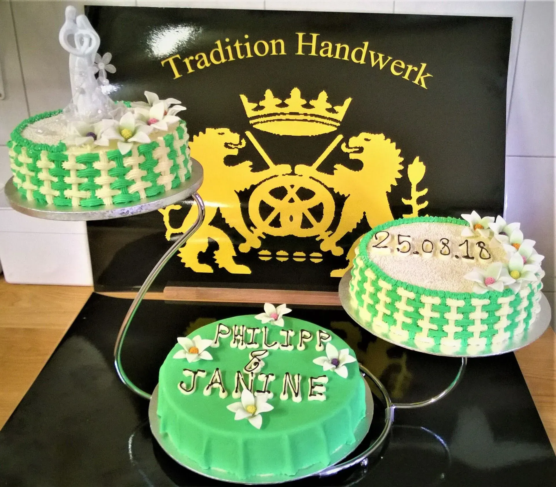 Drei verzierte Kuchen auf einem Tisch vor einem schwarzen Schild mit der Aufschrift „Traditionelles Handwerk“.