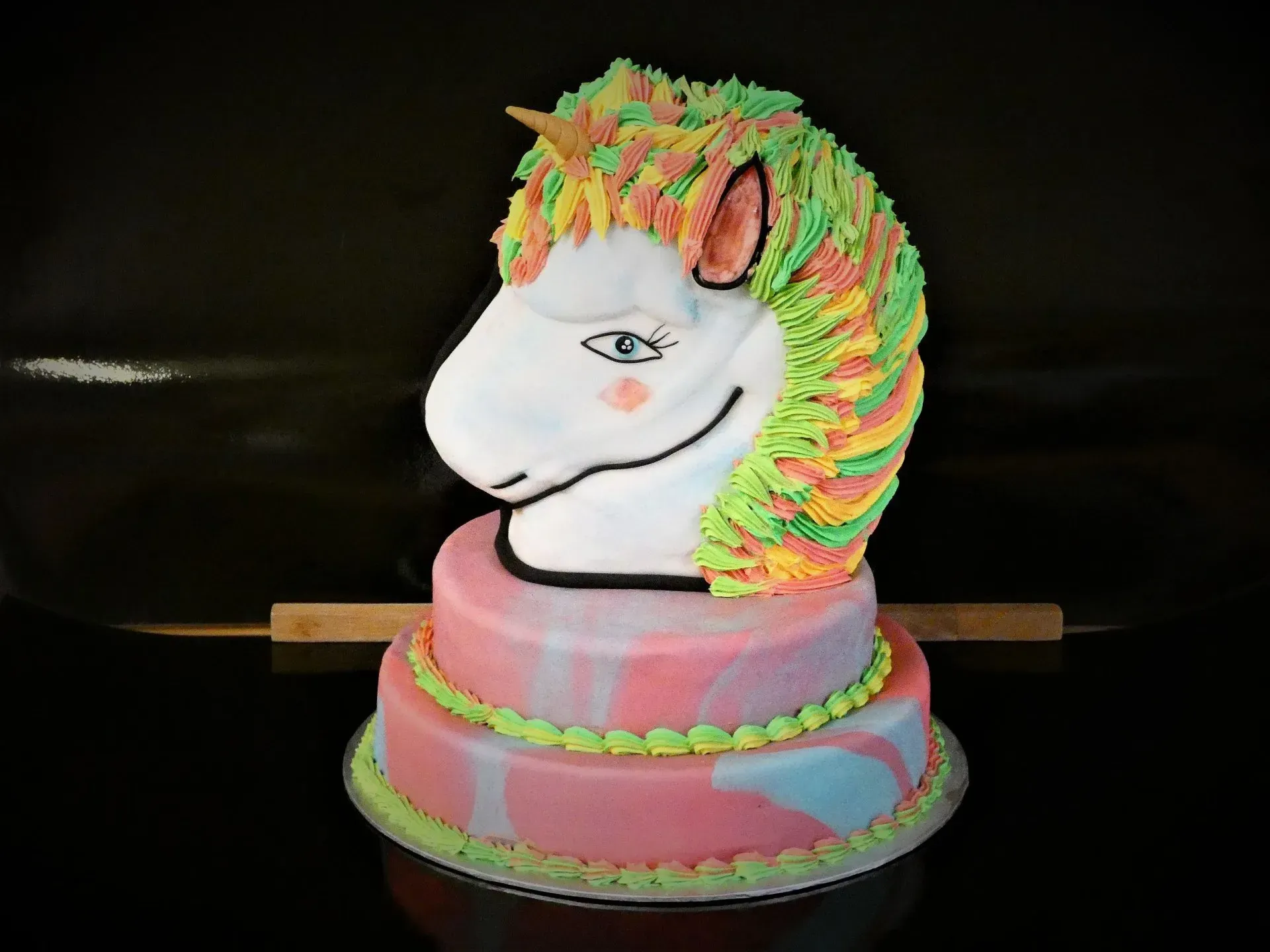 Verzierter, pferdeförmiger Kuchen mit rosa Boden und bunter Mähne auf schwarzem Hintergrund
