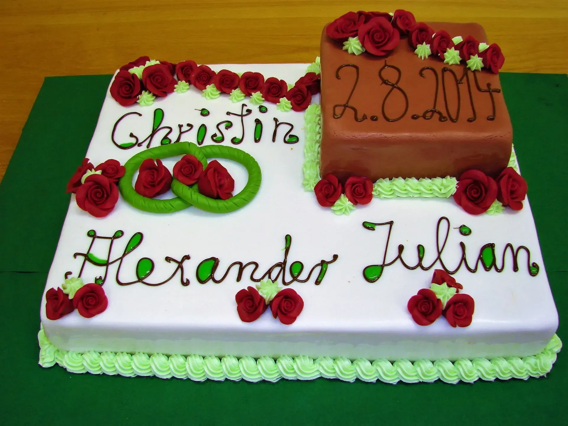 Verzierte weiße und orangefarbene Jubiläumstorte mit roten Rosen und den Aufschriften „Chrisine“ und „Alexander Julian“