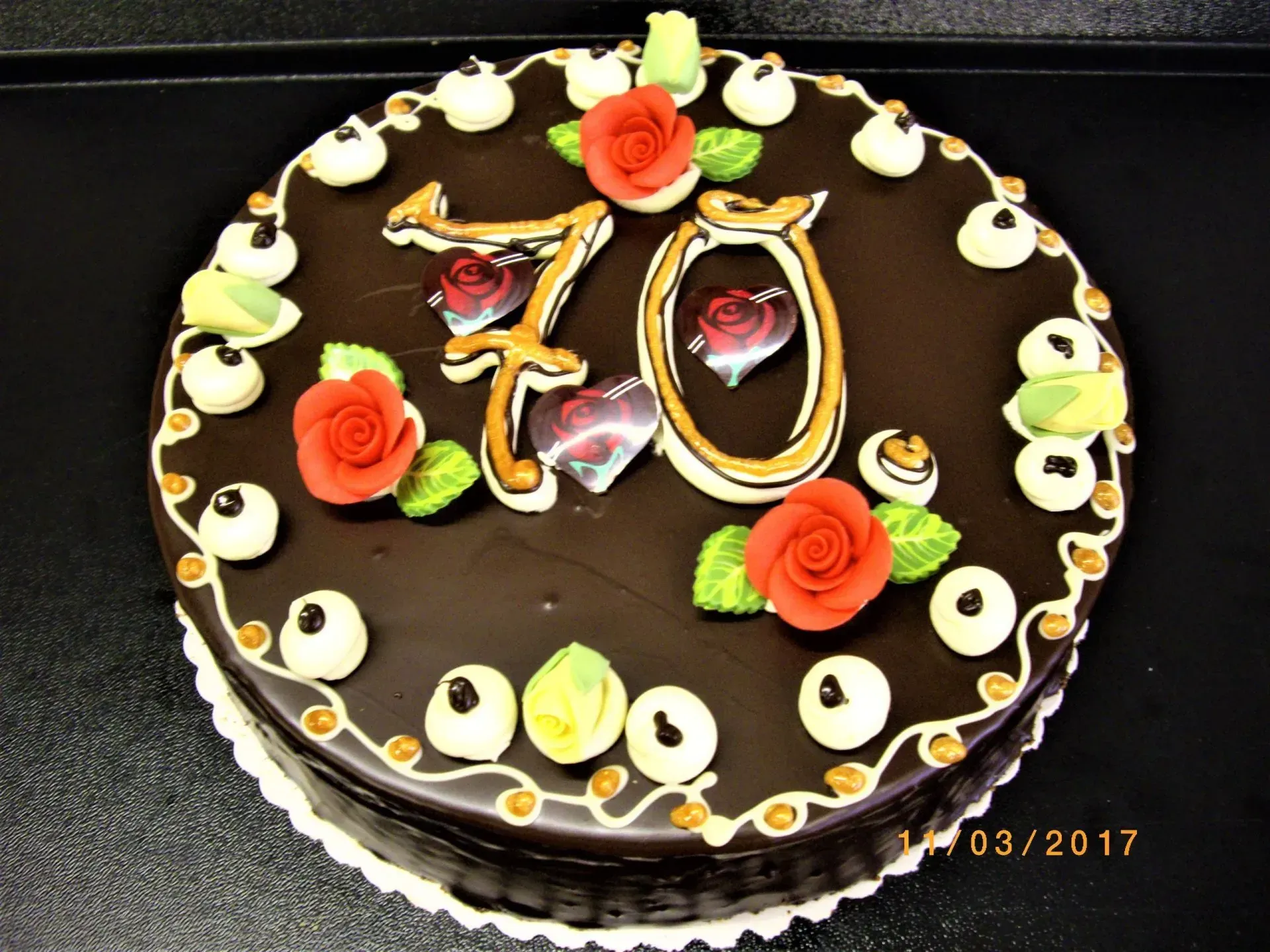 Schokoladengeburtstagstorte mit „70“-Topper, verziert mit orangefarbenen Rosen und weißen Wirbeln