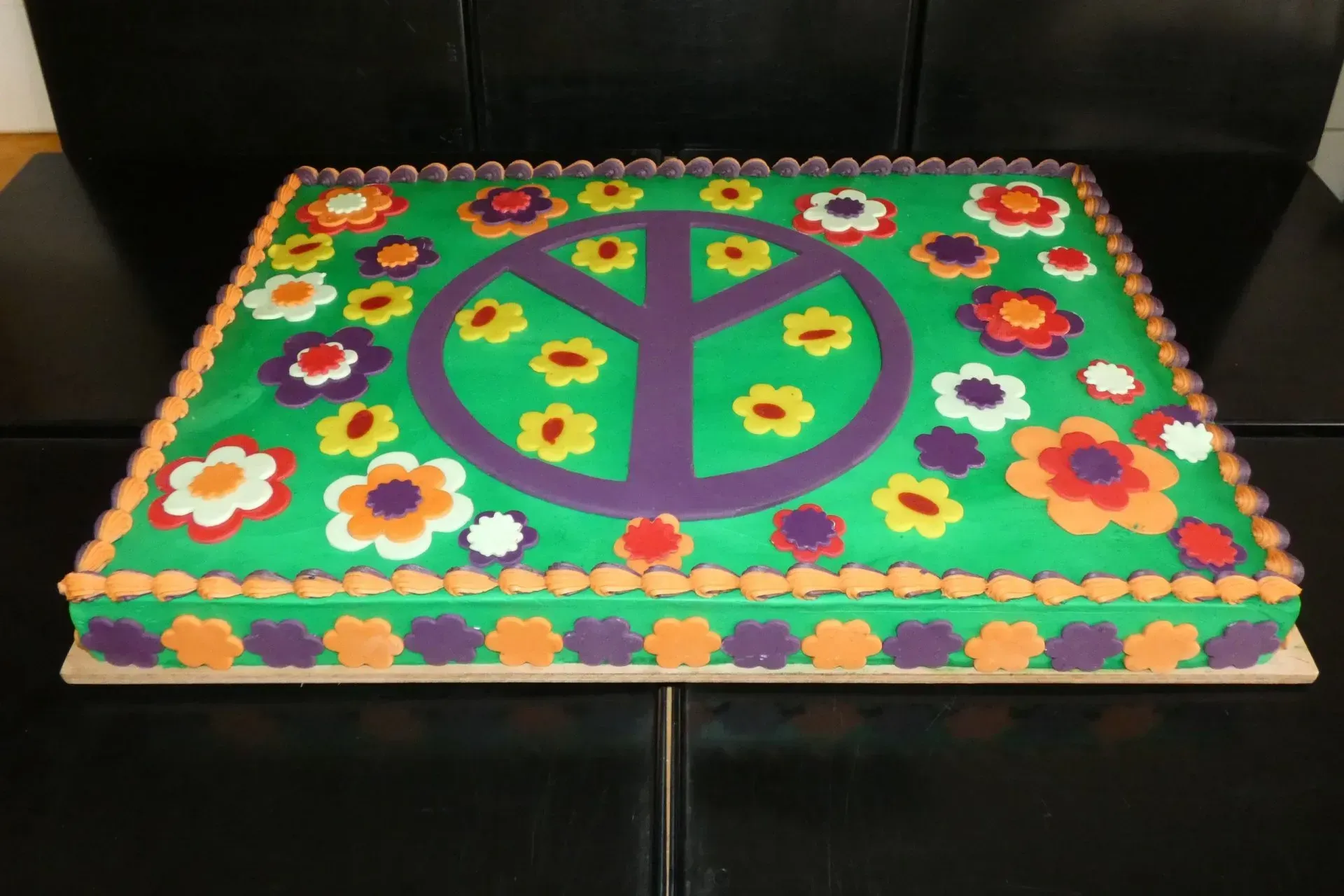Bunte Friedenszeichen-Torte, verziert mit Blumen, auf einer schwarzen, sofaähnlichen Oberfläche
