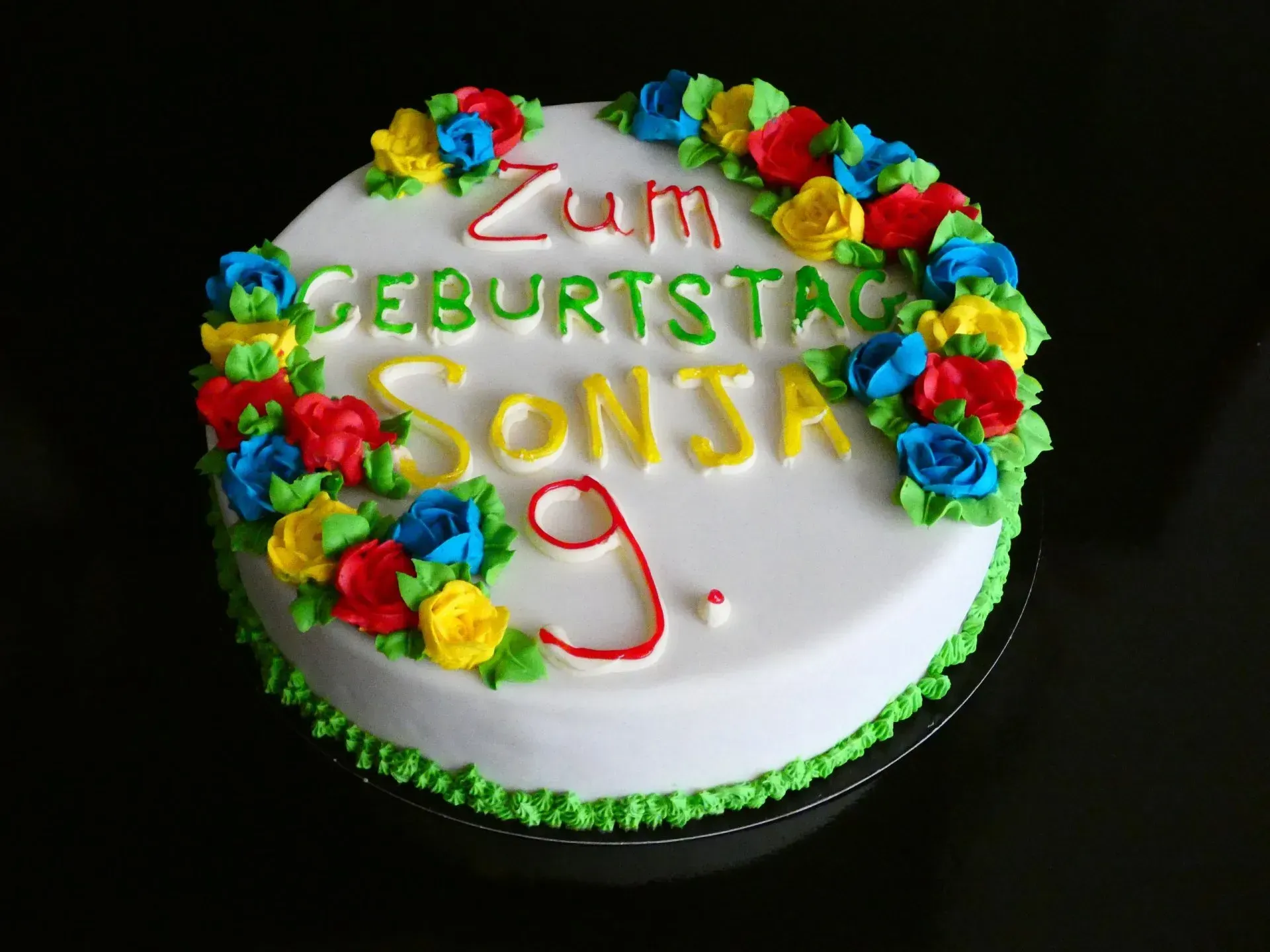 Geburtstagstorte mit bunten Blumen und dem deutschen Schriftzug „Zum Geburtstag Sonja“ sowie einer roten 9