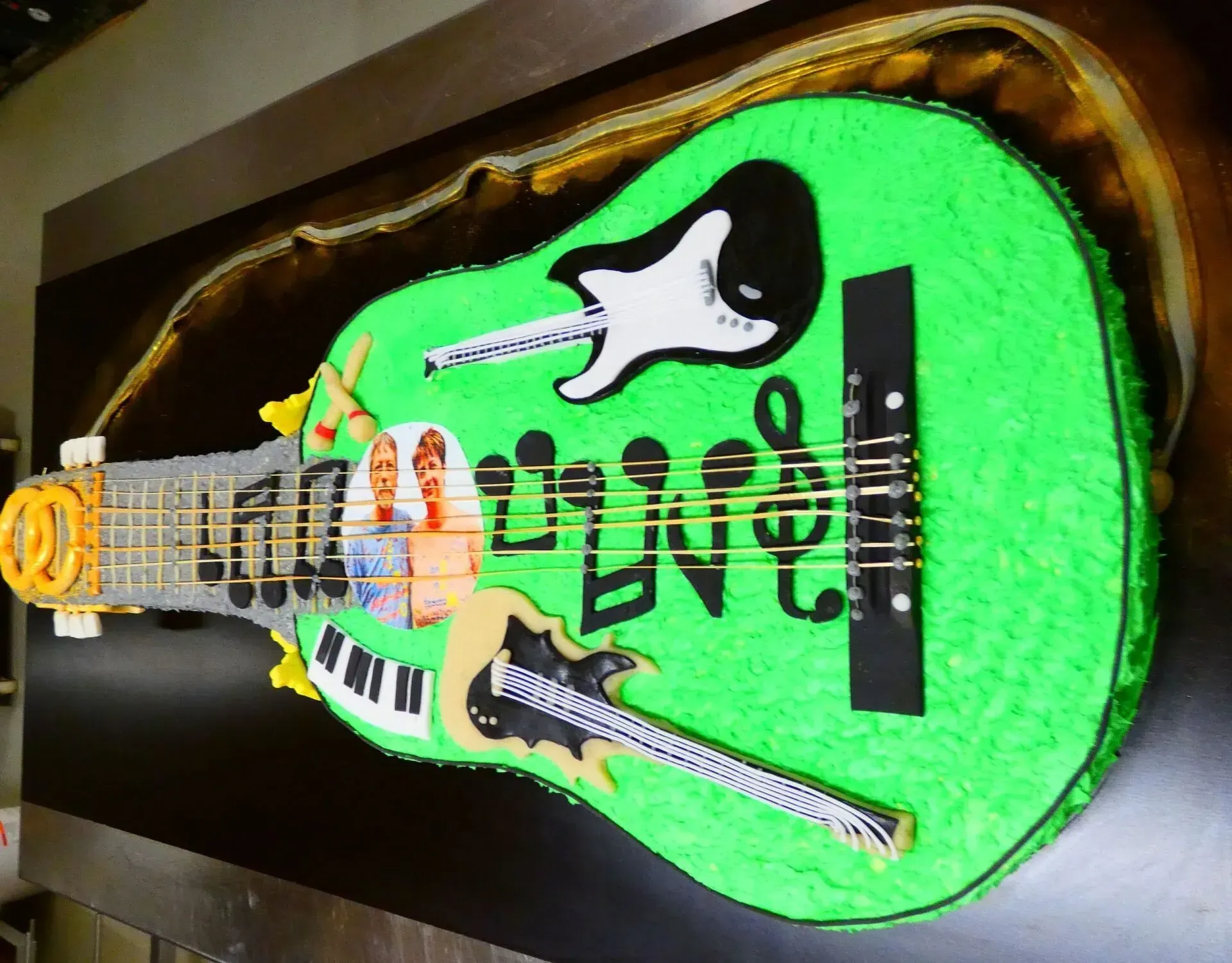 Neongrüner, gitarrenförmiger Kuchen mit schwarz-weißen Details auf dunklem Grund.