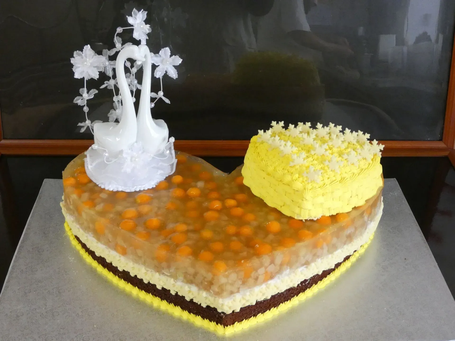 Herzförmiger Schichtkuchen mit orangefarbenem Belag, gelben Blüten und weißer Dekoration.