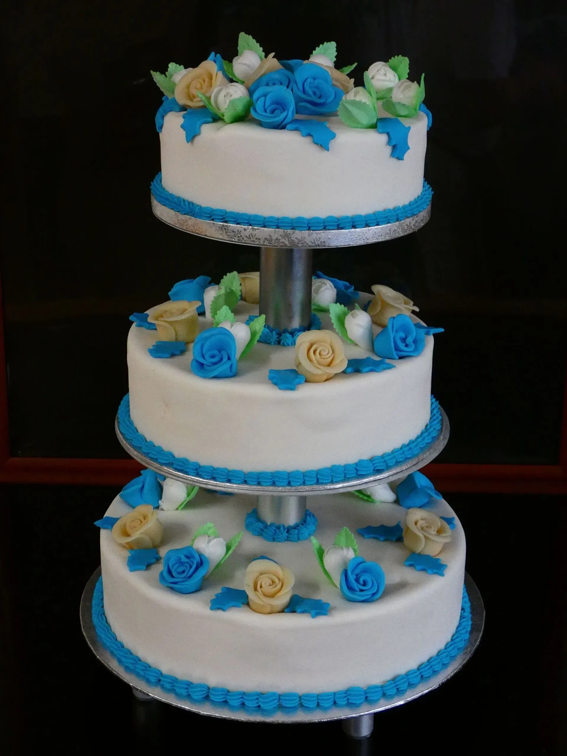 Dreistöckige weiße Torte mit blauem Rand und blau-gelben Blüten auf einem Ständer