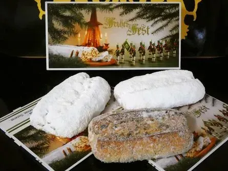 Drei Puderzuckergebäcke und ein glasiertes Gebäck auf einem festlichen Platzdeckchen mit einer festlichen Grußkarte dahinter.