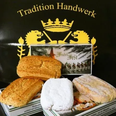 Zwei Puderzuckergebäcke vor einer schwarzen Tasche mit goldenem „Tradition Handwerk“-Wappen und einer Windmühlenszene