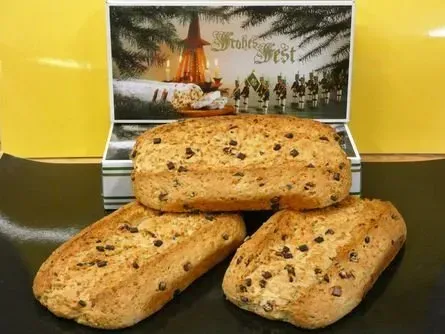 Drei mit Früchten gespickte Brote auf einem Tablett, dahinter ein Schild mit einer malerischen Szenerie.
