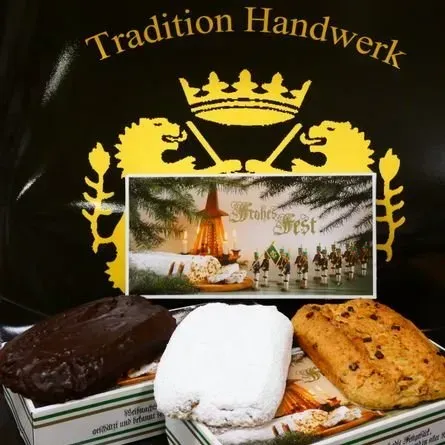 Goldgekröntes „Tradition Handwerk“-Logo mit drei Puderzuckergebäcken auf einem Tablett davor