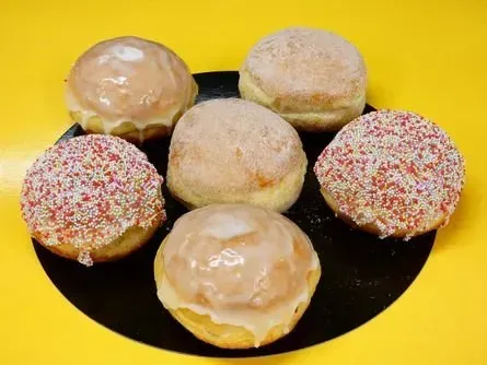 Sechs glasierte Donuts mit Streuseln auf einem schwarzen Teller