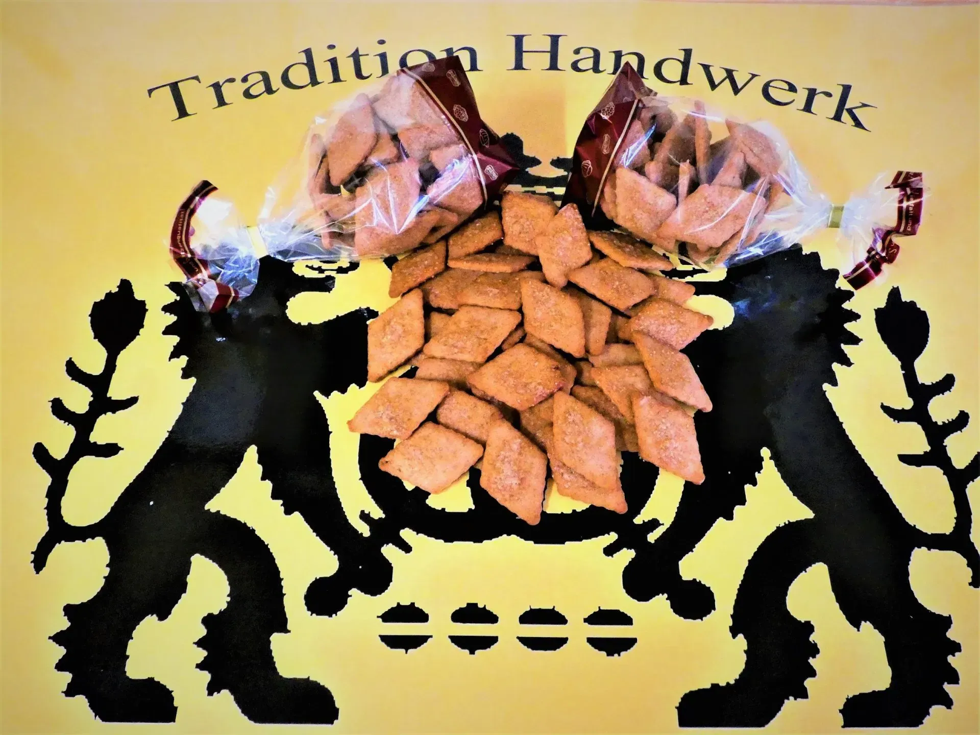 Logo des traditionellen Handwerks mit zwei schwarzen Löwen, Brot und Text auf gelbem Hintergrund