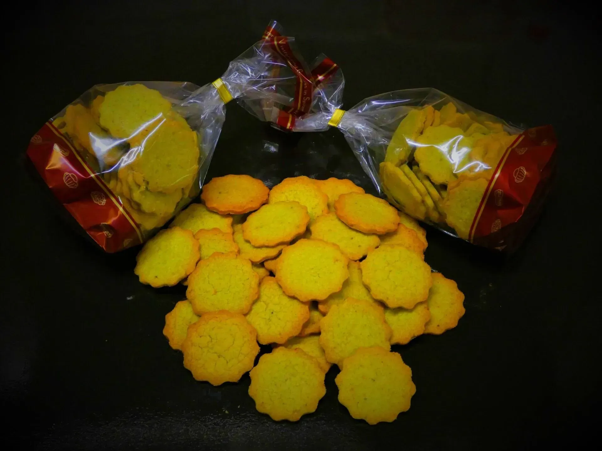 Gelbe Kekse und zwei verpackte Päckchen auf schwarzem Hintergrund