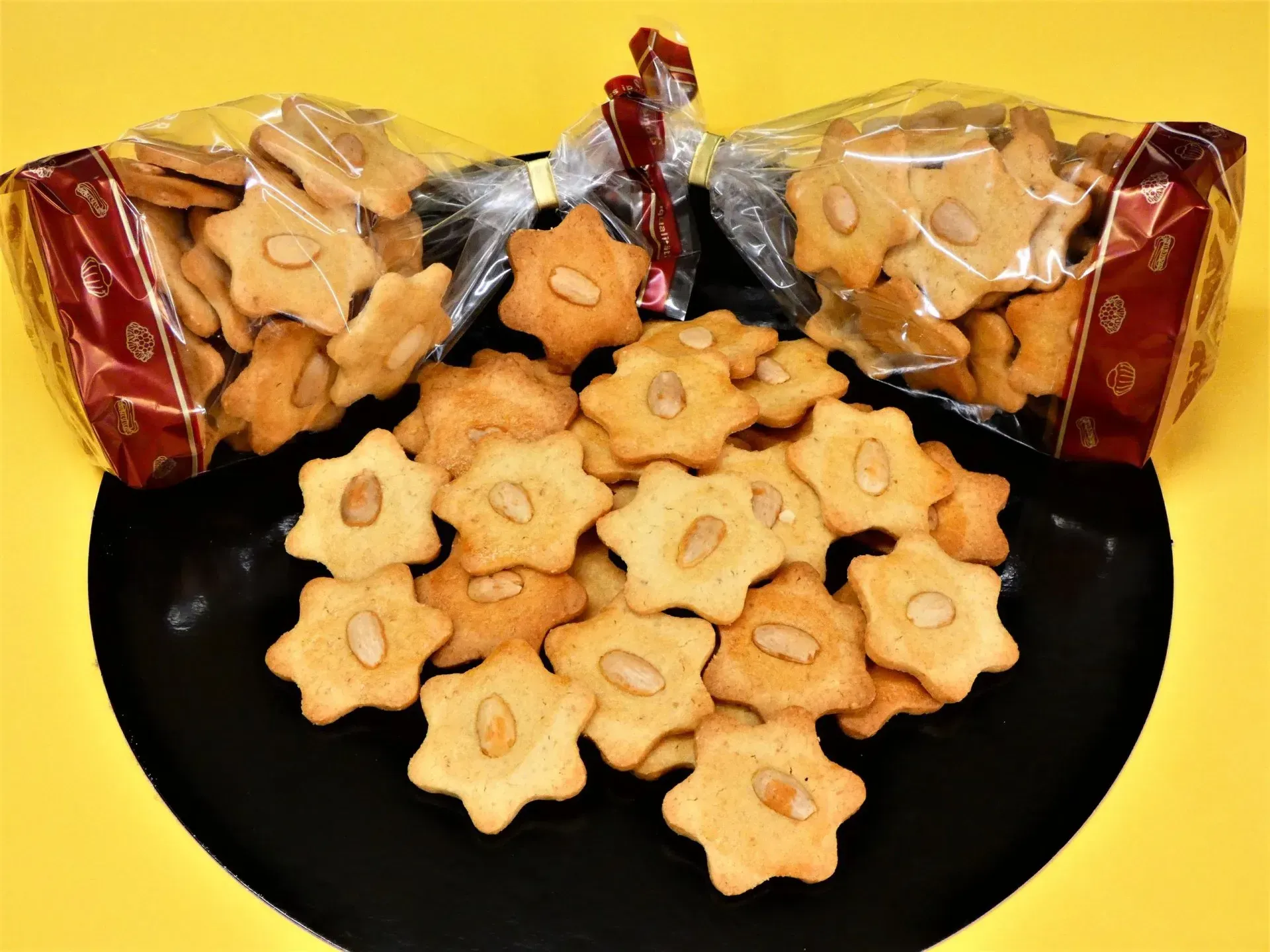 Sternförmige Butterkekse auf einem schwarzen Teller, daneben zwei offene Snacktüten auf gelbem Hintergrund