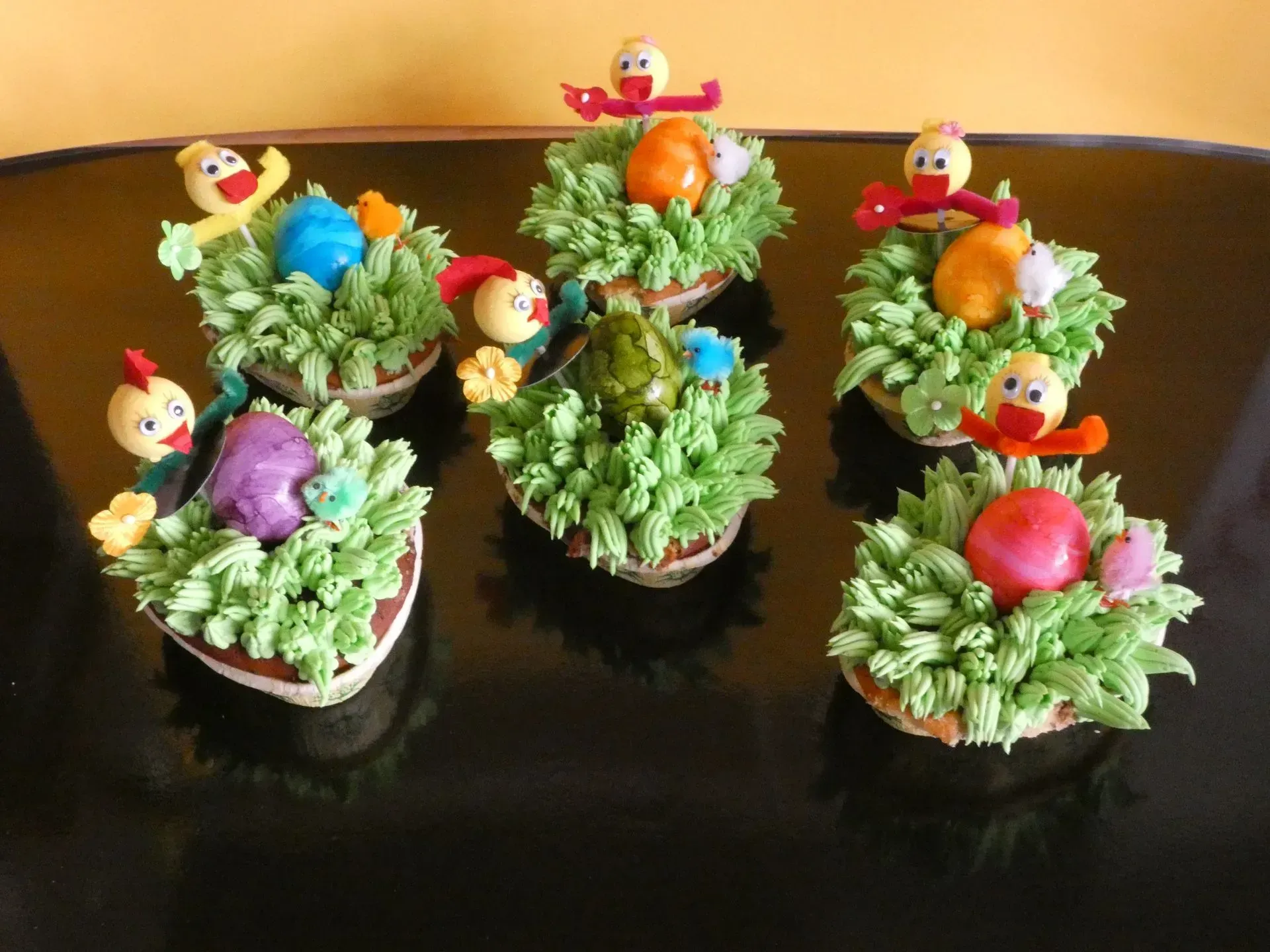 Bunte Blumen-Cupcakes mit Küken-Dekorationen auf schwarzem Grund