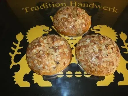Drei Körnerbrötchen auf einem schwarzen Tablett mit goldenem Löwenmotiv und dem Schriftzug „Tradition Handwerk“.