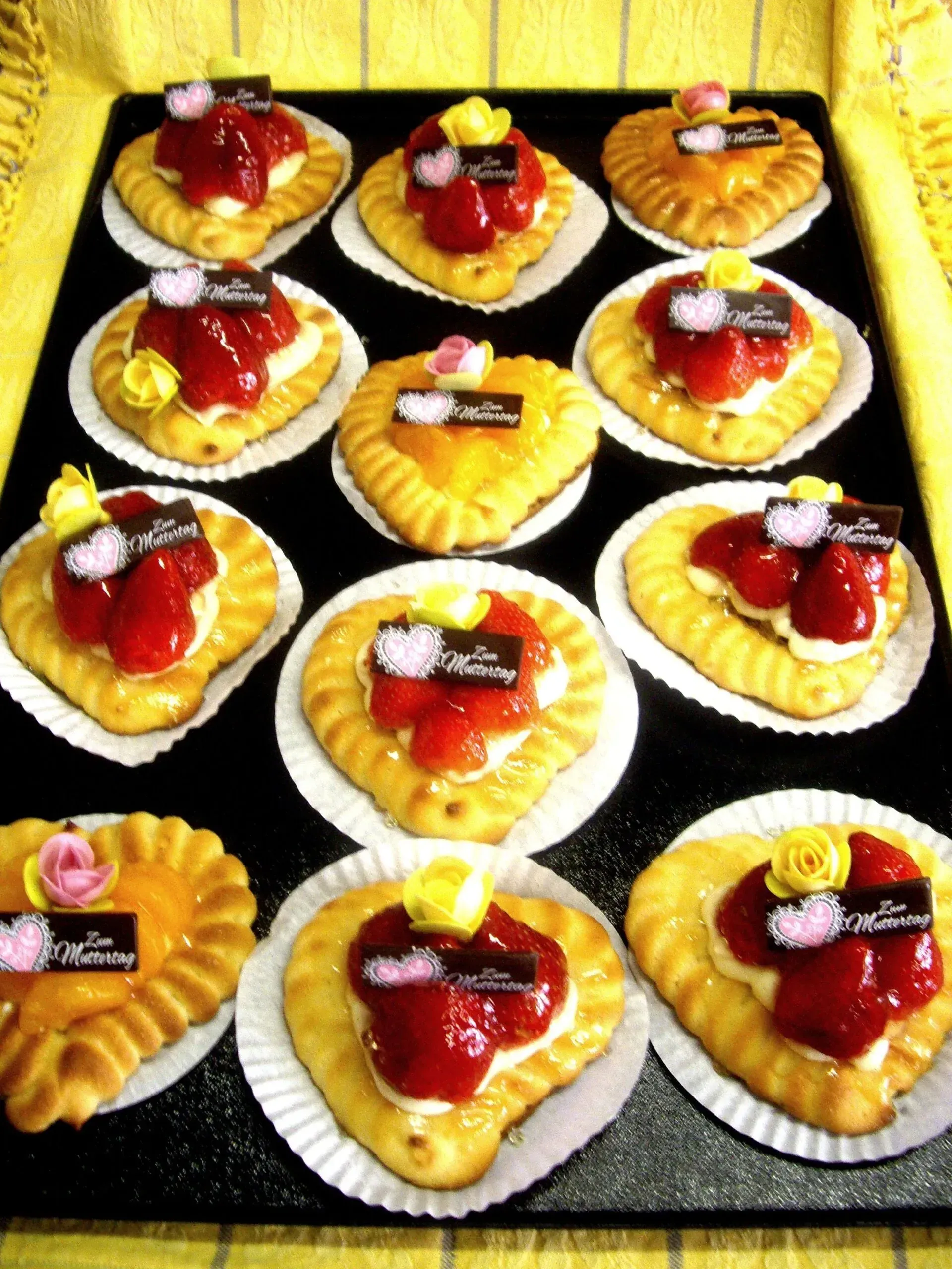 Herzförmige Obsttörtchen mit roter Gelee und Kirschen, auf einem Tablett angerichtet.