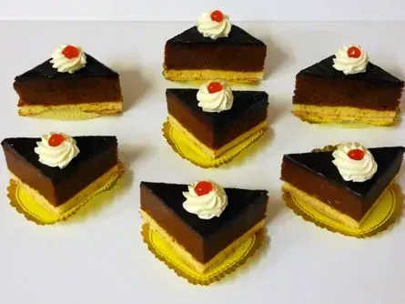 Sechs mit Schokolade überzogene Kuchenstücke mit weißen Sahnewirbeln auf hellem Hintergrund.