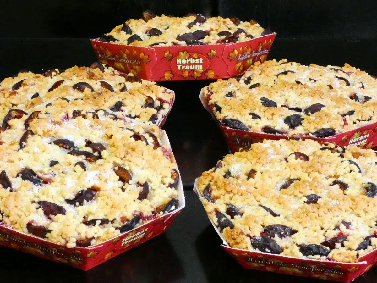 Vier mit Beeren belegte Streuselkuchen in roten Backformen auf einer schwarzen Oberfläche