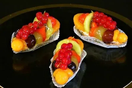 Drei kleine Obsttörtchen mit roten Johannisbeeren, Weintrauben und Kiwischeiben auf einem schwarzen Teller