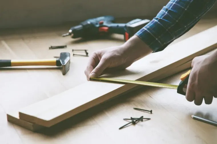 Persona midiendo una tabla de madera con una cinta métrica, rodeada de herramientas.
