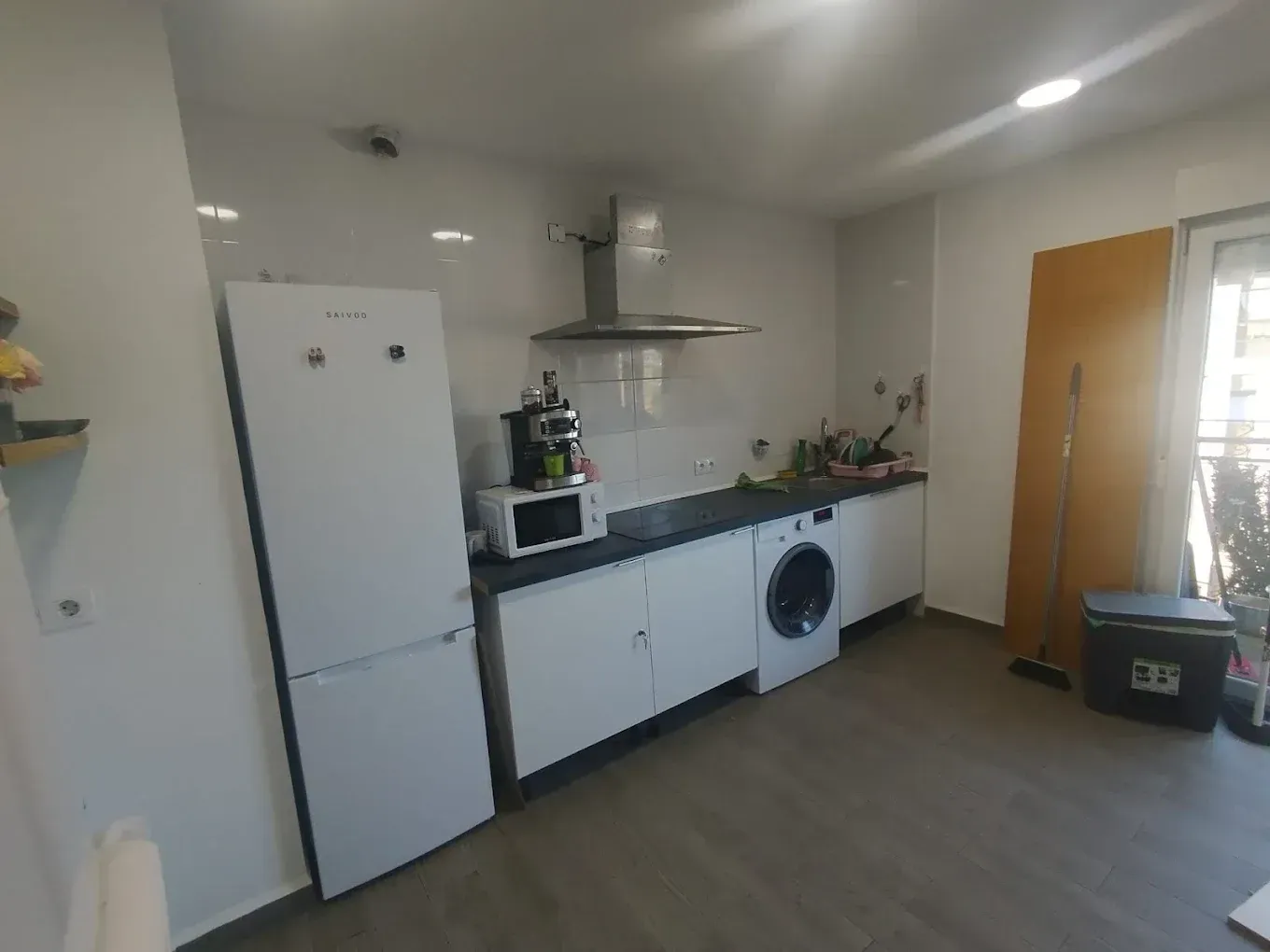 Cocina blanca con frigorífico, armarios y electrodomésticos; se ve una lavadora.