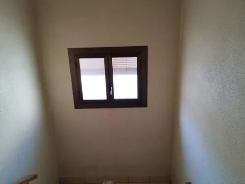 Ventana marrón con persianas en una pared beige encima de las escaleras.
