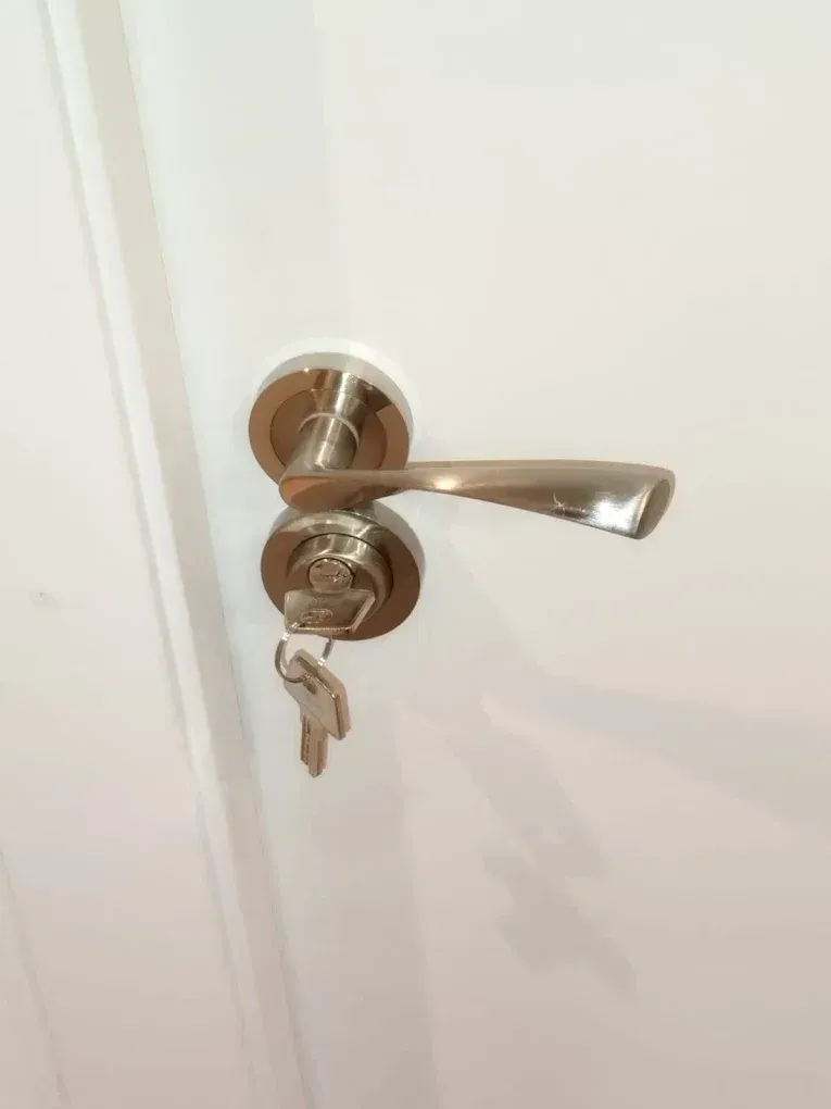Pomo y cerradura plateados en una puerta blanca. Las llaves están insertadas en la cerradura.