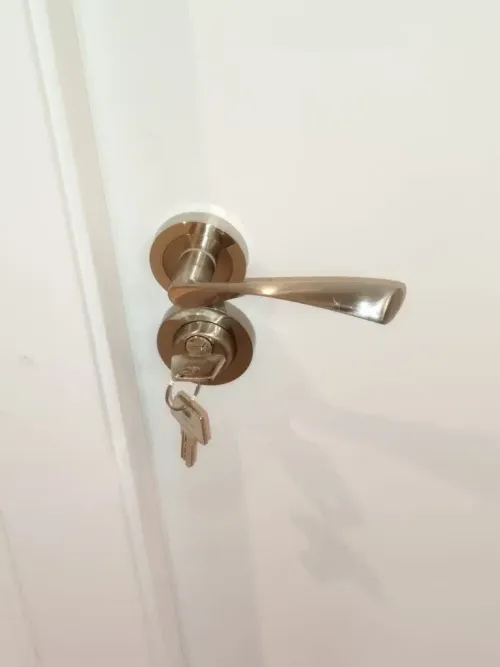 Pomo y cerradura plateados en una puerta blanca. Las llaves están insertadas en la cerradura.