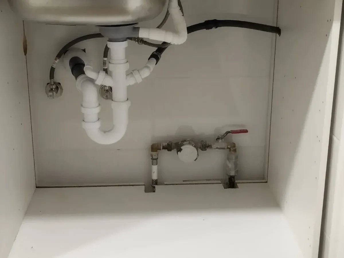 Instalación de fontanería bajo el fregadero: tuberías blancas, fregadero y válvula. Tubería de desagüe negra visible.