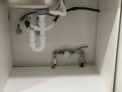 Instalación de fontanería bajo el fregadero: tuberías blancas, fregadero y válvula. Tubería de desagüe negra visible.